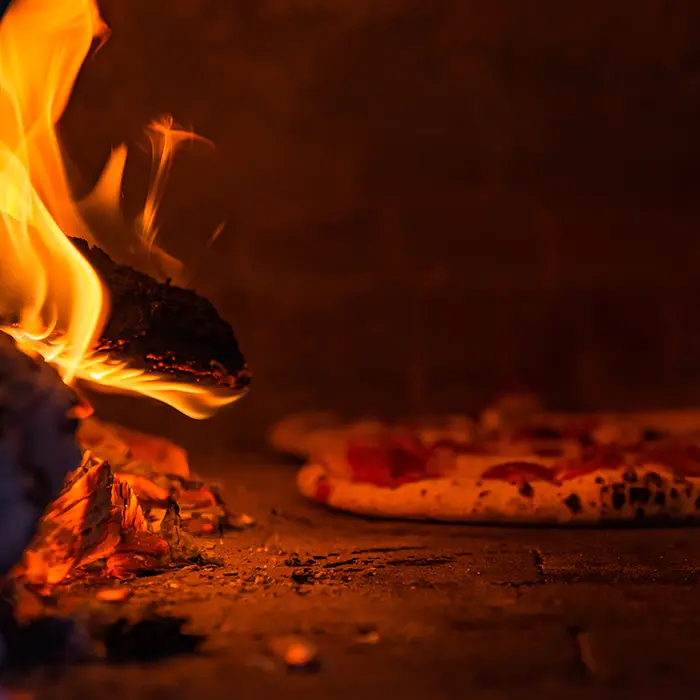 Flames beside a pizza baking on the floor of a wood-fired oven
