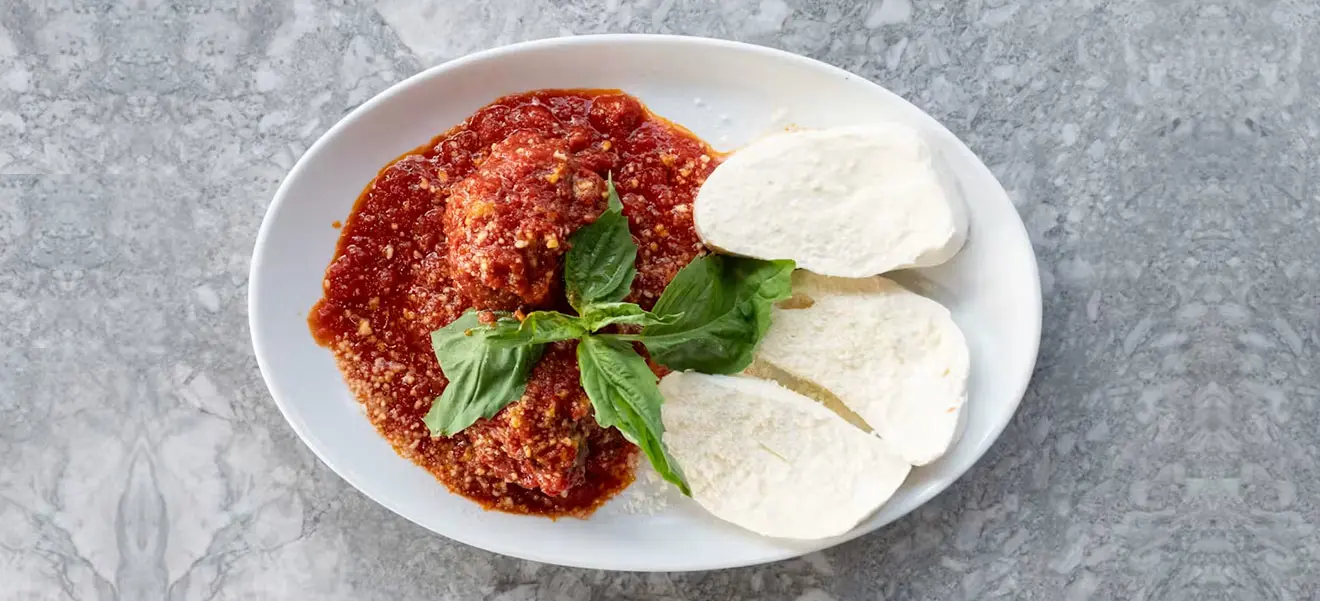 Meatballs in tomato sauce with fresh mozzarella and basil on a white plate