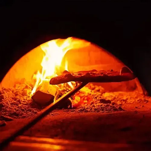A pizza on a peel in a glowing wood-fired oven