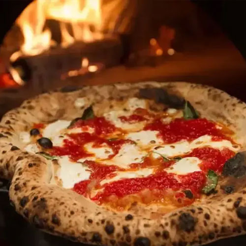 A Neapolitan-style margherita pizza in front of the oven fire