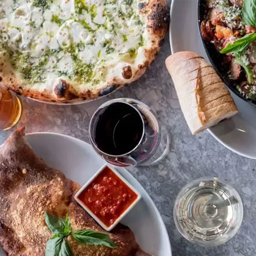 A spread of pizza, bread, red wine and dishes on a marble table