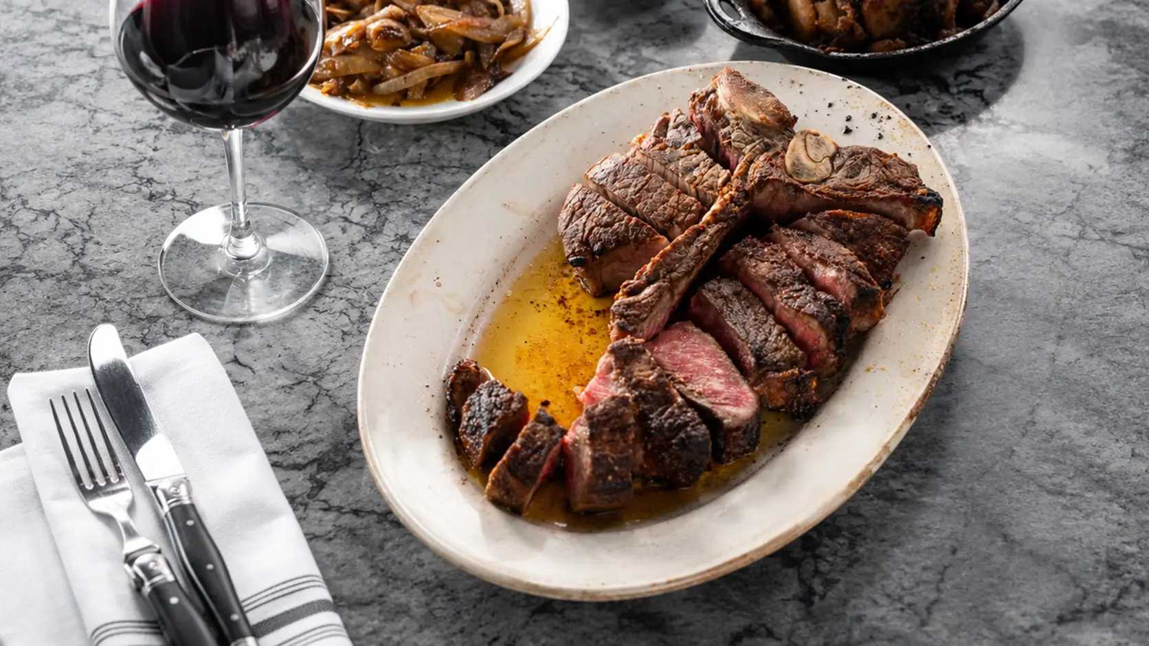 A sliced dry-aged porterhouse with a glass of red wine
