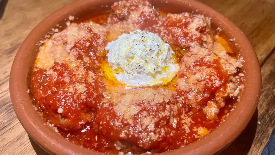 Meatballs in marinara topped with ricotta in a terracotta dish