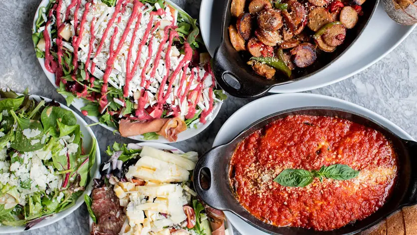 A spread of salads, sausage and peppers, and baked dishes on a marble table