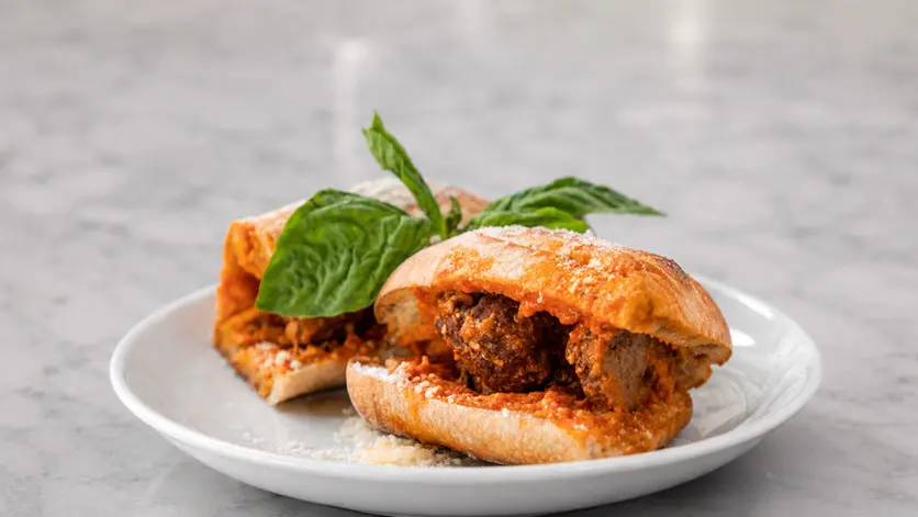A meatball sandwich with fresh basil on a white plate