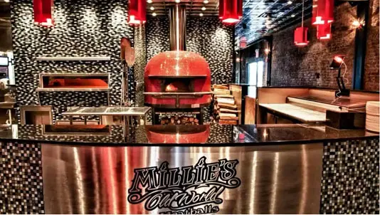 Millie’s Old World dining room and bar with the red pizza oven behind