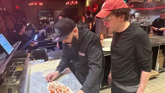 Pizza maker stretching dough as a guest watches at the pizza counter