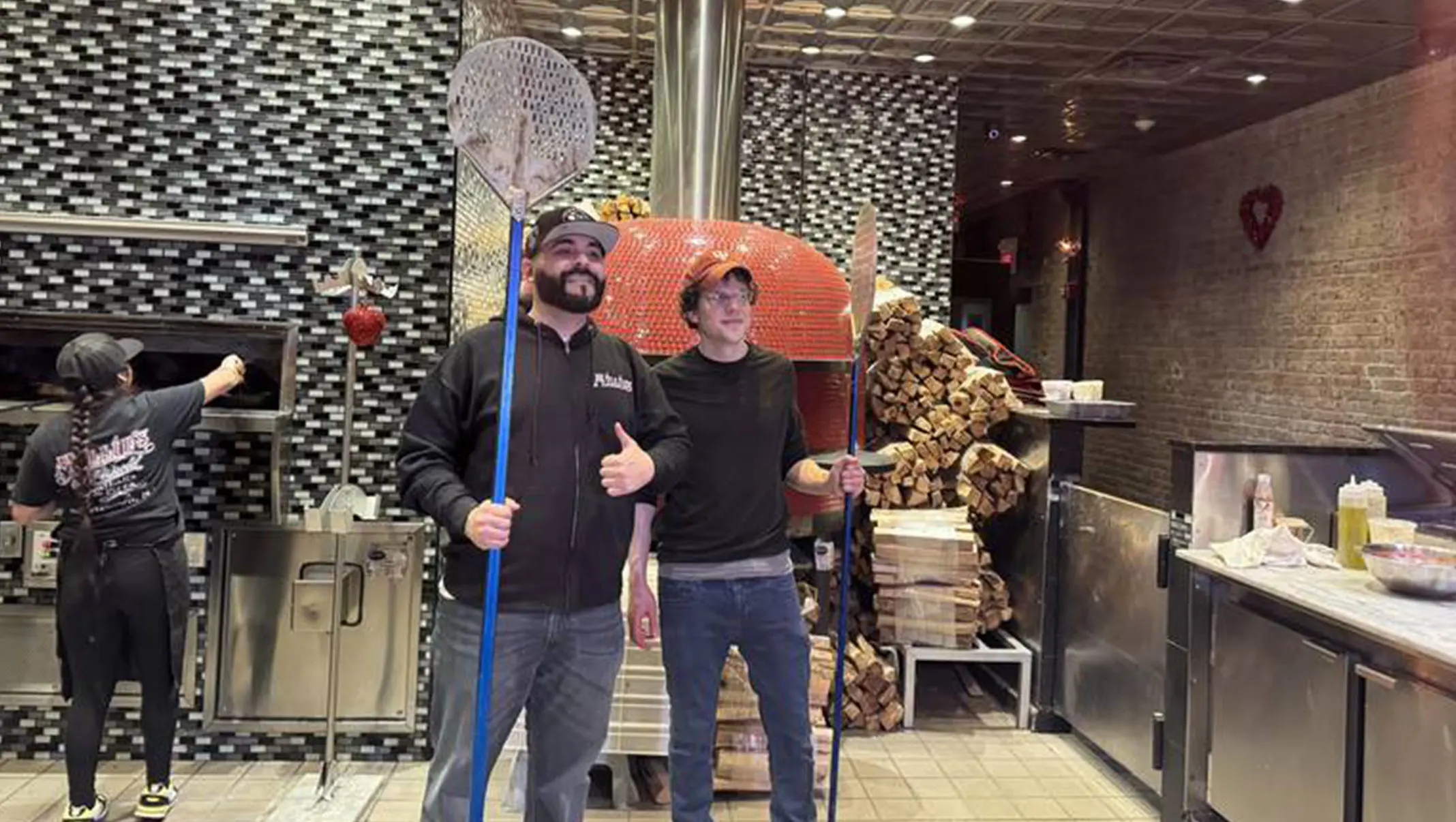 Pizza makers holding a pizza peel beside the oven in the Millie’s kitchen