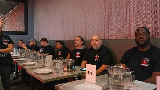 Meatball-eating contest participants seated along a table in the dining room