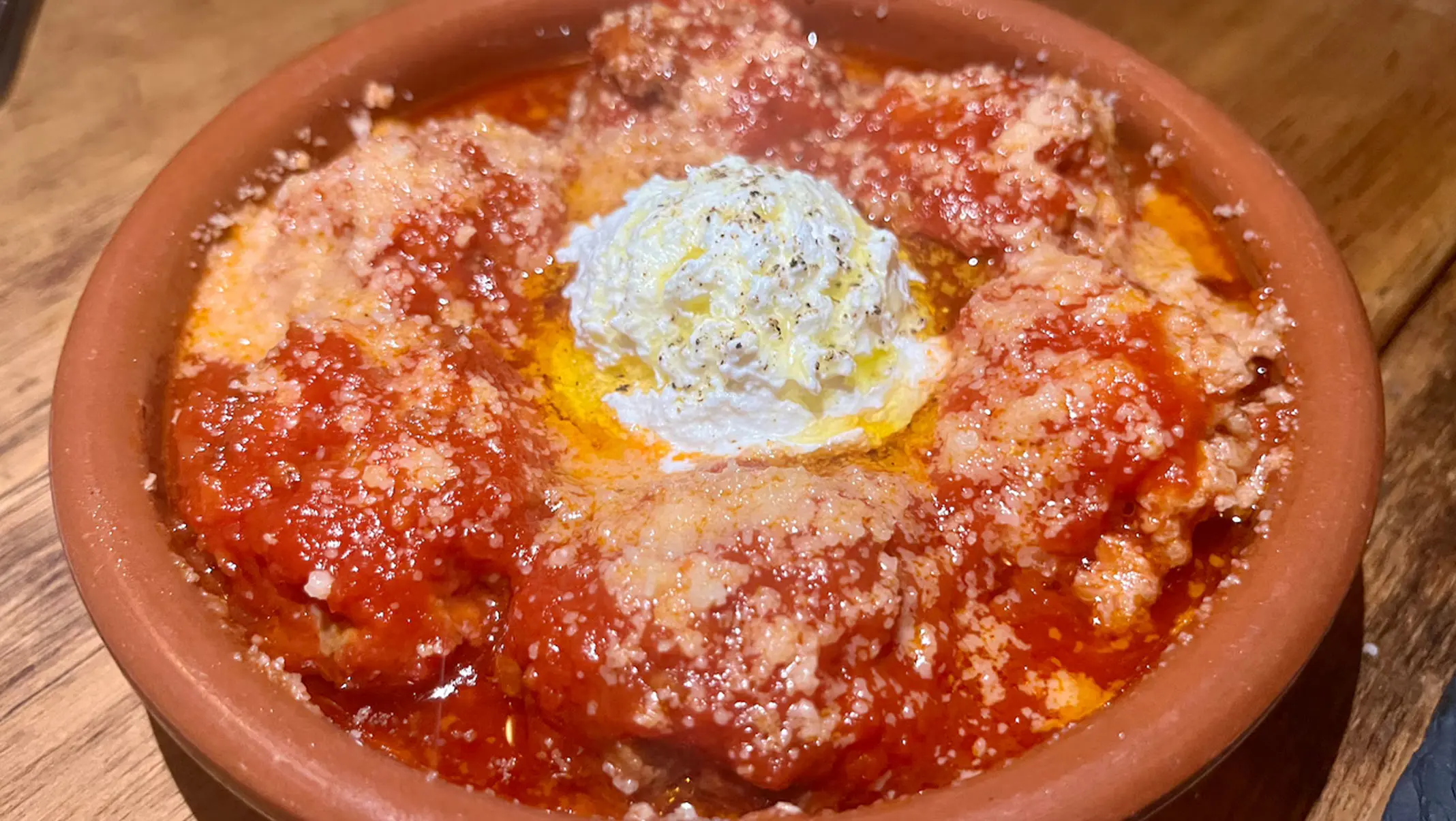 Meatballs in tomato sauce topped with ricotta in a terracotta dish