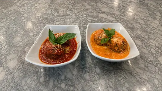 Two bowls of meatballs in tomato and vodka sauces with fresh basil