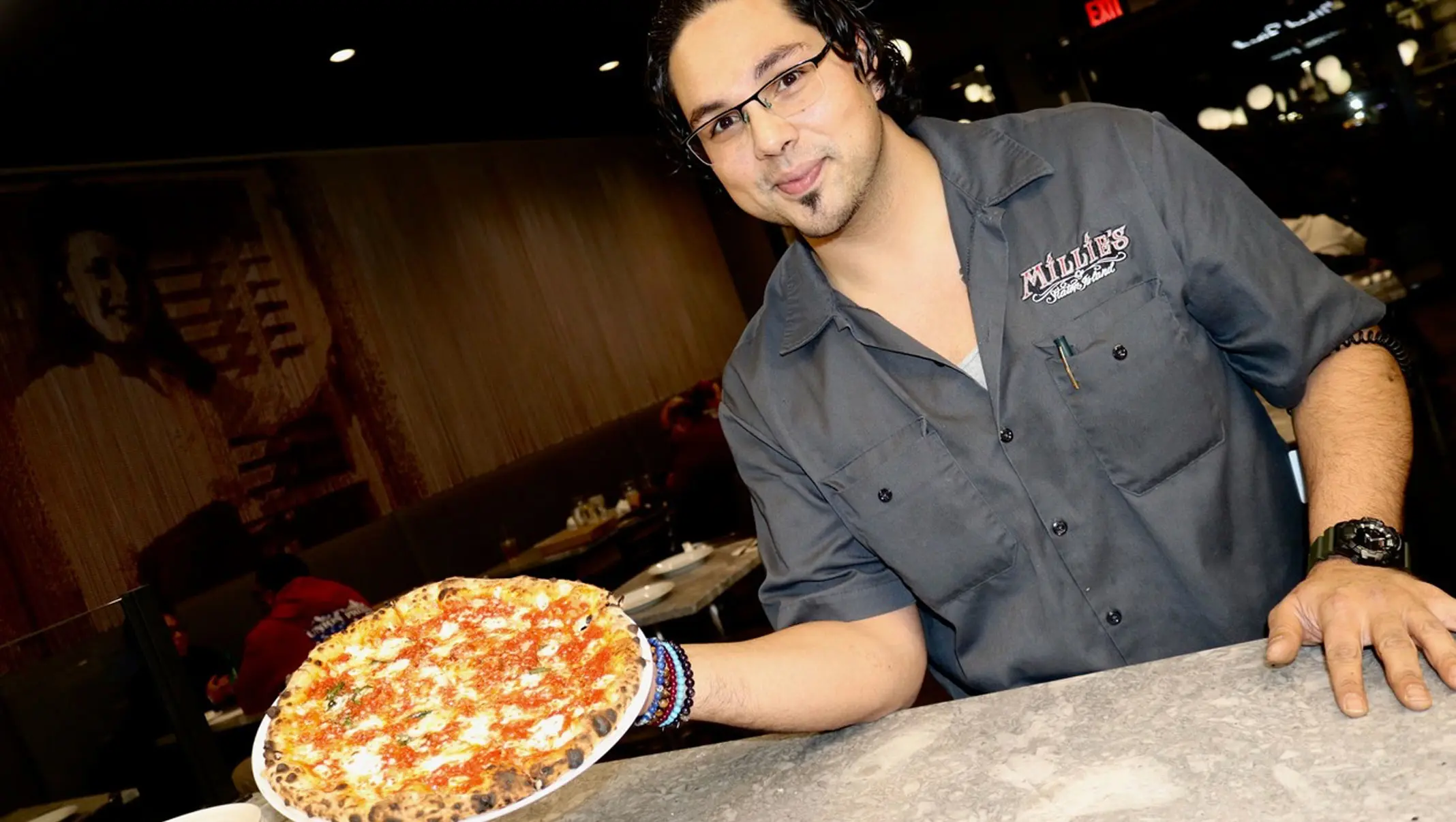 Chef in a Millie’s shirt holding a pizza at the counter