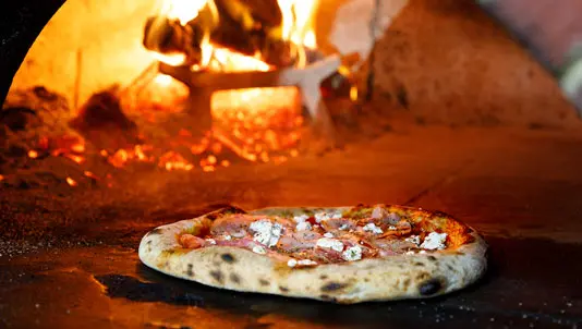 Pizza baking in front of the glowing fire of a wood-fired oven
