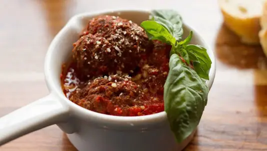 Meatballs in a white serving dish with fresh basil