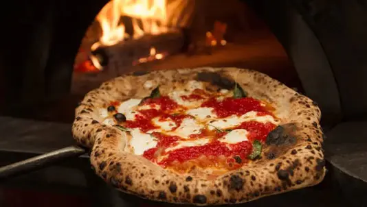 Pizza on a peel in front of a wood-fired oven