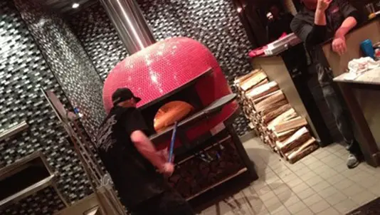 Pizza maker working at the red-tiled pizza oven
